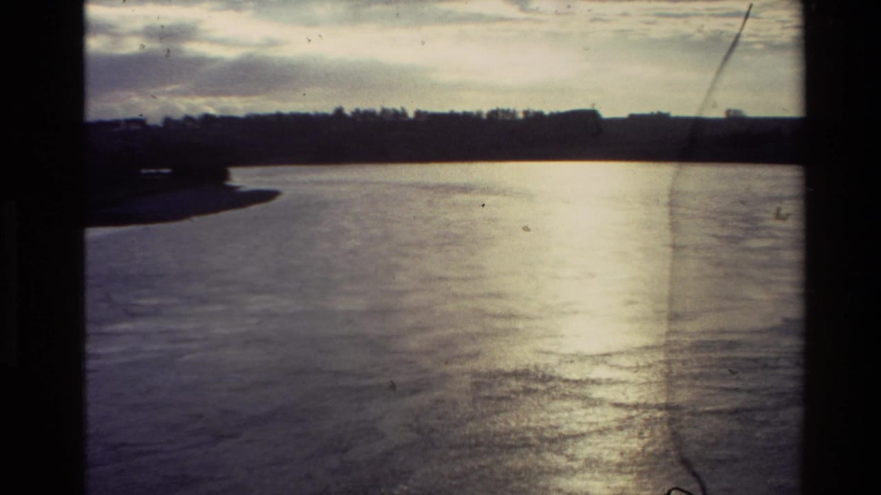 Wide river bend with dark tree line, cloudy sky, and bright reflection on the water.