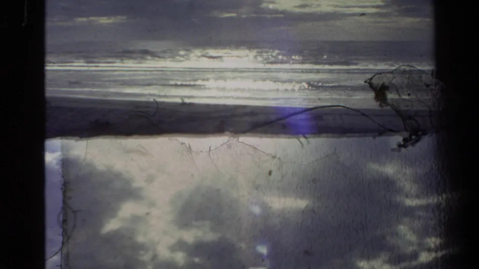 1981 New Zealand 8mm frame with bright ocean reflection, a dark shore strip, bluish lens flare, and visible film wear.