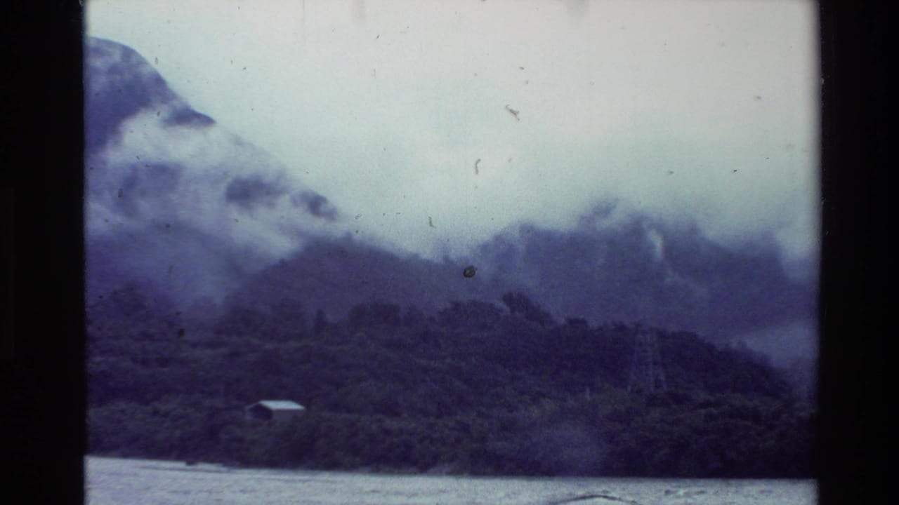 Fog-covered mountain and forested shoreline with a small structure near the water.