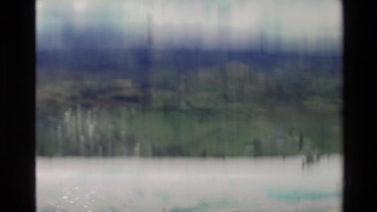Blurred lake or shoreline view with distant green hills and vertical film streaking.