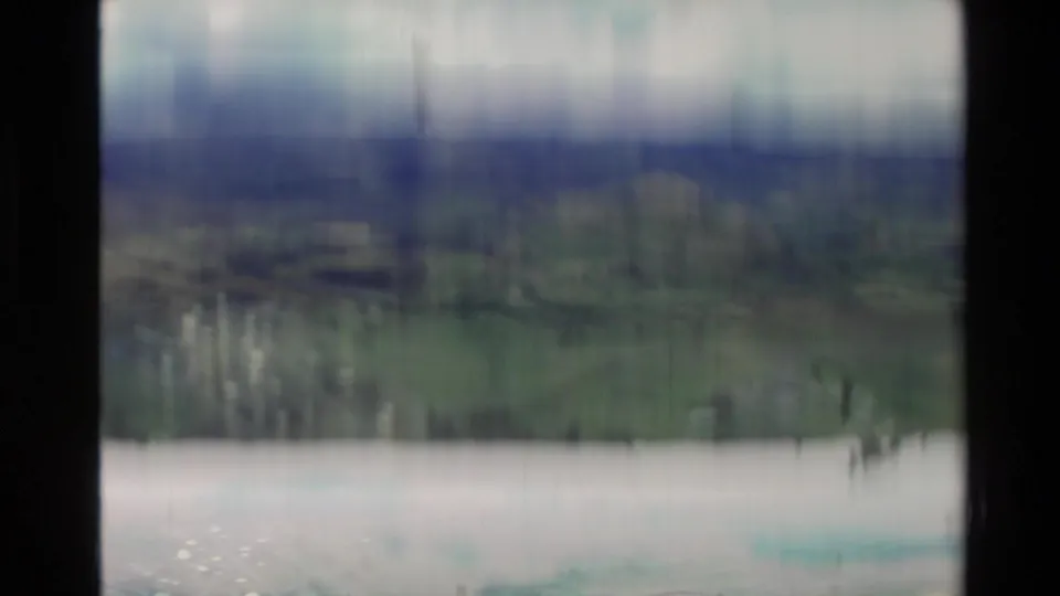 Soft, unstable 8mm view in New Zealand showing pale water, distant vegetation and blurred hills under cloud.