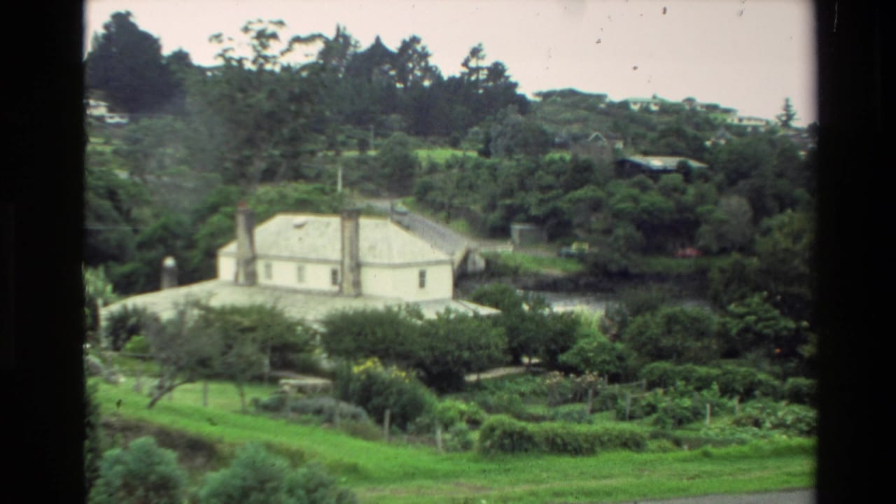 1981 New Zealand 8mm frame showing a distant white house set in a wooded hillside landscape with gardens in front.