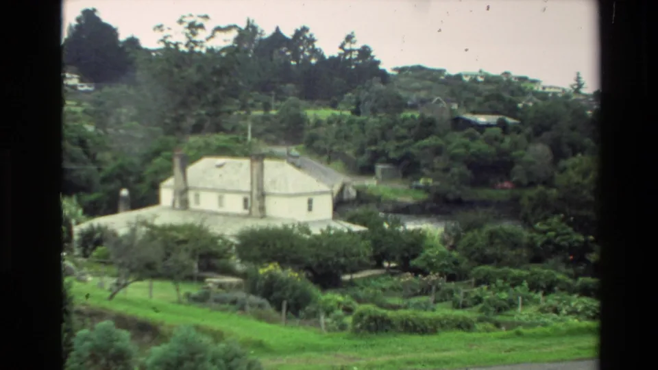 1981 New Zealand 8mm frame showing a distant white house set in a wooded hillside landscape with gardens in front.