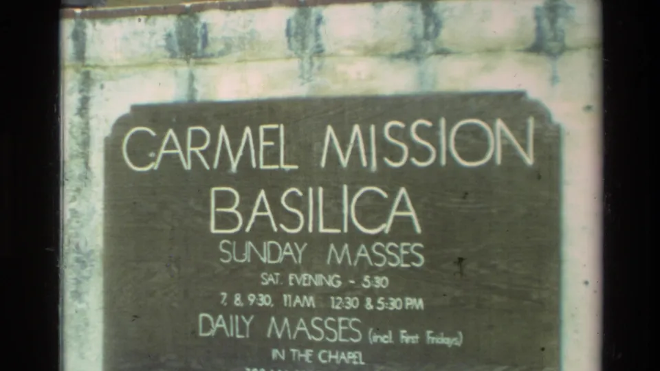 Carmel Mission Basilica sign in Carmel, California, showing Sunday mass times and daily masses in the chapel.