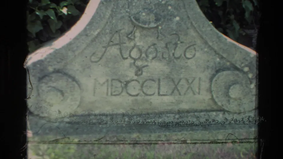 Carmel, California 1982 home-movie frame showing a weathered stone garden marker inscribed Agosto MDCCCLXXI near shaded greenery.