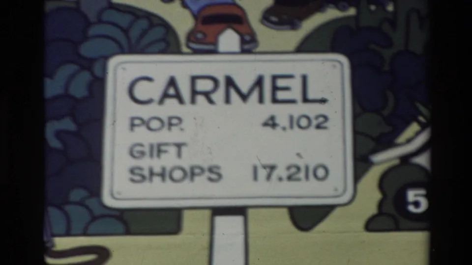 1982 Carmel, California home-movie frame showing a filmed cartoon sign with population and gift-shop numbers against a colorful illustrated backdrop.