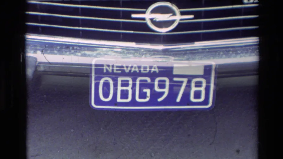 Close 8mm frame of a vehicle grille with an Oldsmobile emblem and a Nevada license plate reading OBG978.