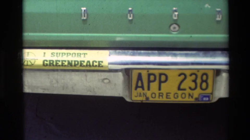1982 Carmel home-movie frame showing an Oregon plate on a green car beside an I SUPPORT GREENPEACE bumper sticker.