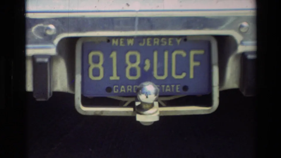 Close view of a New Jersey Garden State plate reading 818 UCF, with tow hardware and chrome bumper visible.