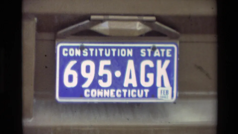 Blue Connecticut Constitution State plate reading 695 ACK on a tan rear vehicle panel in the 1982 Carmel footage.