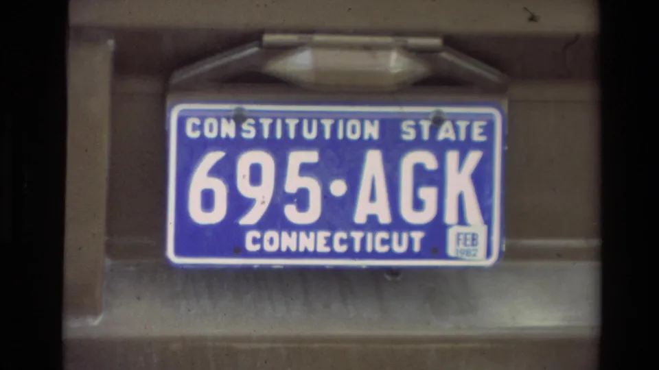 Close-up of a Connecticut license plate with a 1982 registration sticker on a vehicle, seen in 8mm home-movie footage.