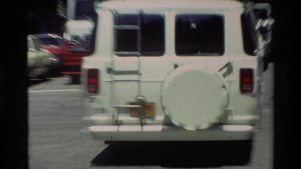 Rear view of a white van with a spare tire and small rear plate, filmed on a street during the Carmel, California travel sequence.