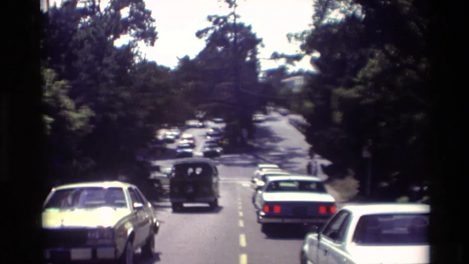Cars travel along a tree-lined roadway in Carmel, California, with the white van visible among other period vehicles.