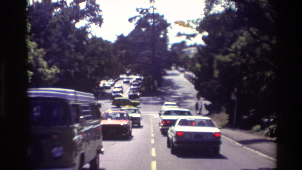 Carmel, California traffic scene from 1982 showing sedans and a van on a sunlit, tree-lined roadway.