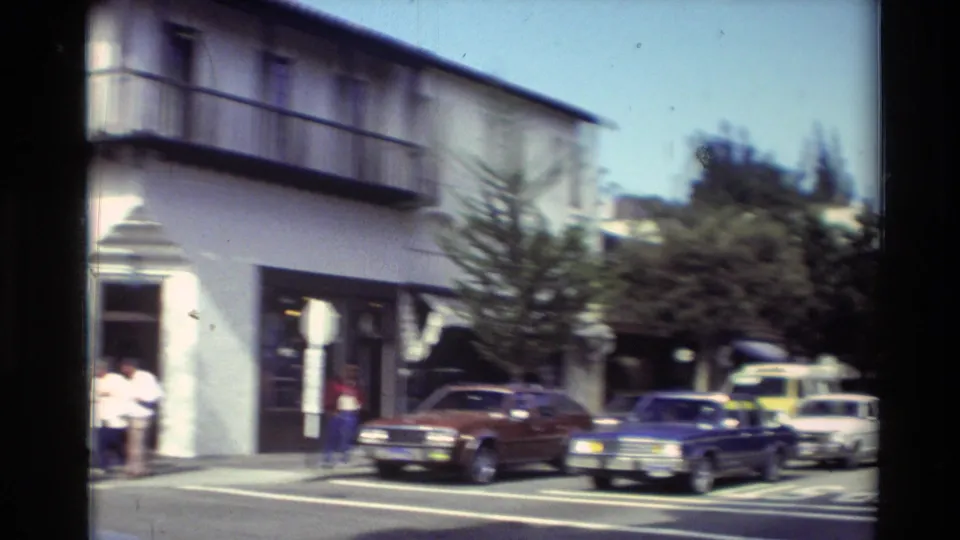 1982 Carmel street view showing a white building with balcony, storefront windows, pedestrians, and parked cars along the curb.
