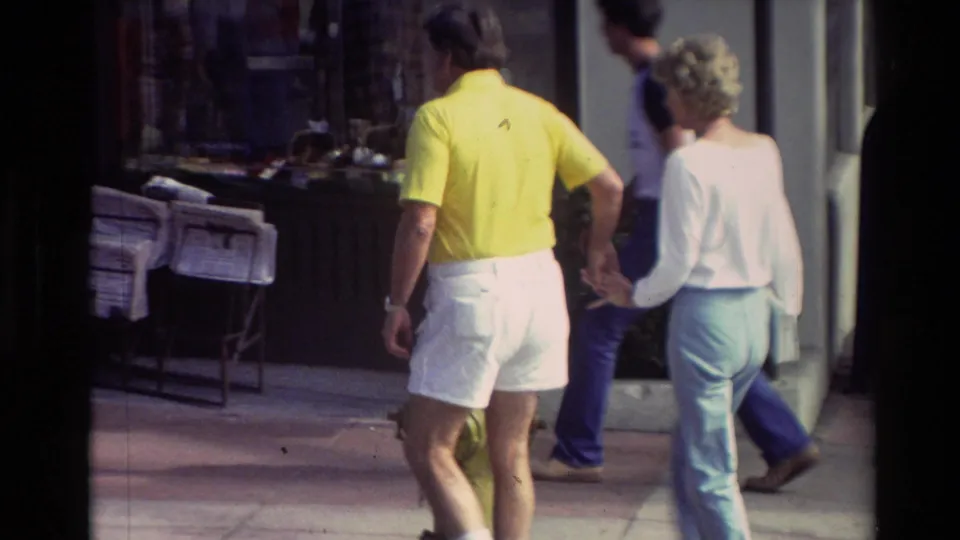 The home-movie camera follows the couple from behind as they continue along a Carmel sidewalk past shop displays in 1982 footage.