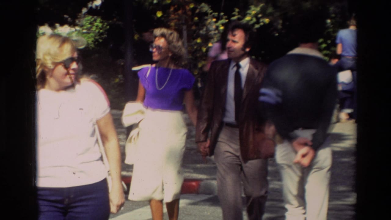 A woman in a purple top and a man in a brown jacket walk among other pedestrians.