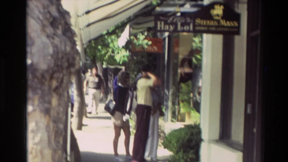 A Carmel street view shows pedestrians near shopfronts and hanging business signs in 1982 home-movie footage.