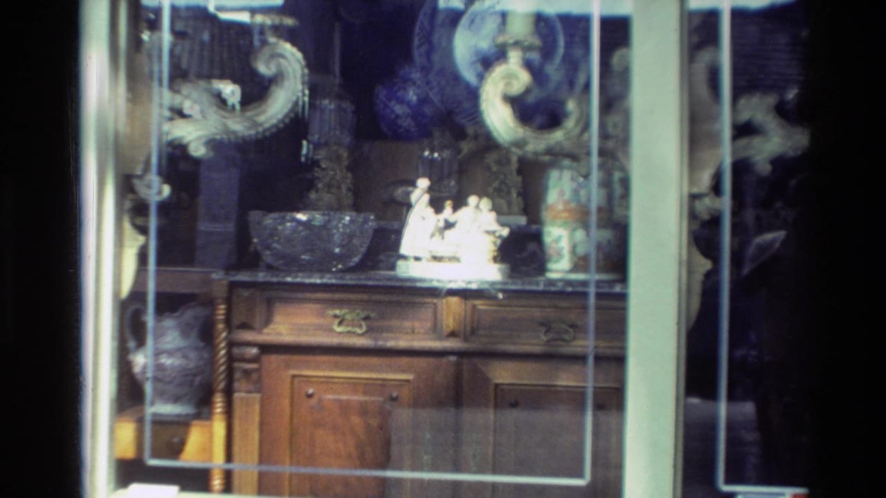 Store window with a wood cabinet, decorative bowl, porcelain vases, and small white figurines behind reflective glass.