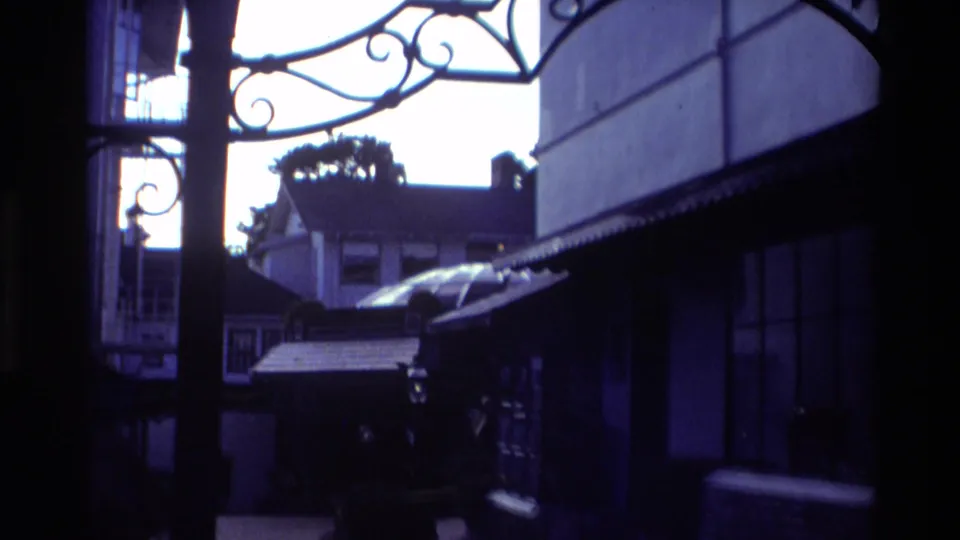 Carmel, California 1982 view from near a shop window, with decorative ironwork, an awning, dark reflections, and buildings across the street.