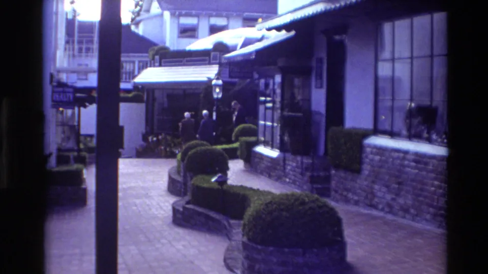 1982 Carmel courtyard view with brick paving, low hedges, shopfront windows, awnings, and pedestrians moving through the passage.