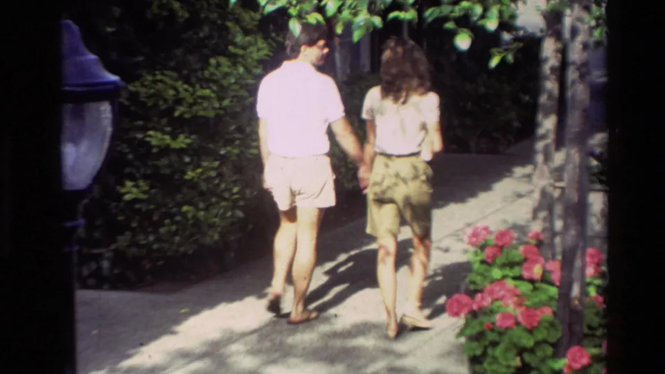 A couple in casual clothing walks hand in hand through a Carmel walkway lined with flowering plants.