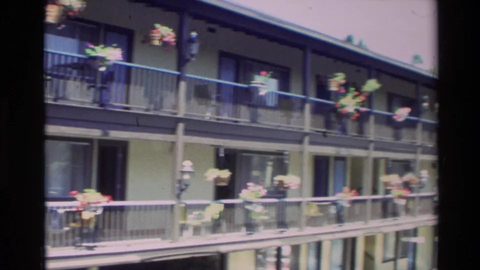 1982 Carmel apartment exterior with two levels of balconies, dark railings, windows, and colorful hanging flowers.
