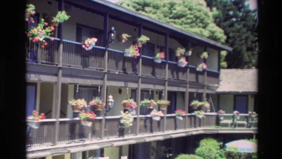 Angled 1982 view of a Carmel apartment block with flower baskets along upper and lower balcony railings.