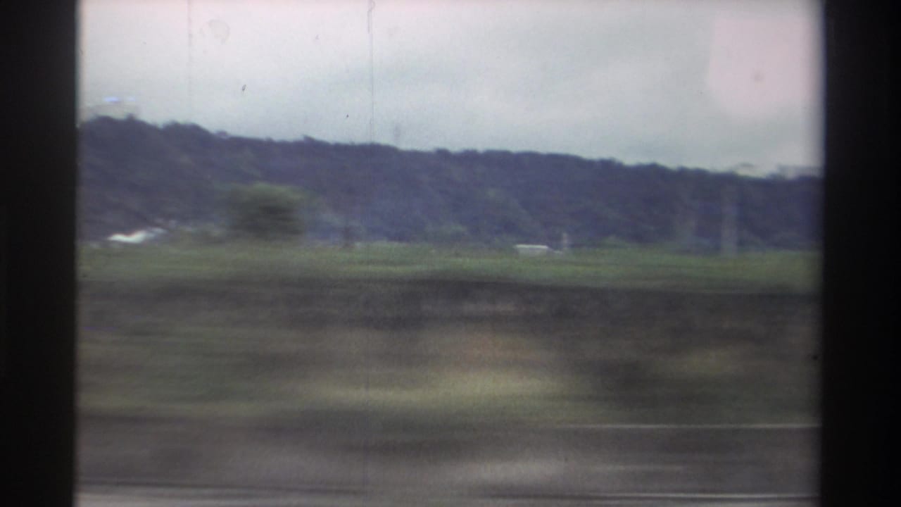 Blurred green fields and wooded hills seen from a moving vehicle.