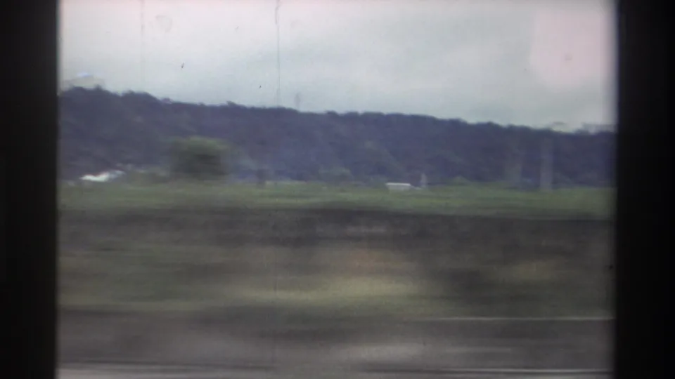 1982 Taiwan home-movie frame showing green fields and tree-covered hills through motion blur from a moving vehicle.