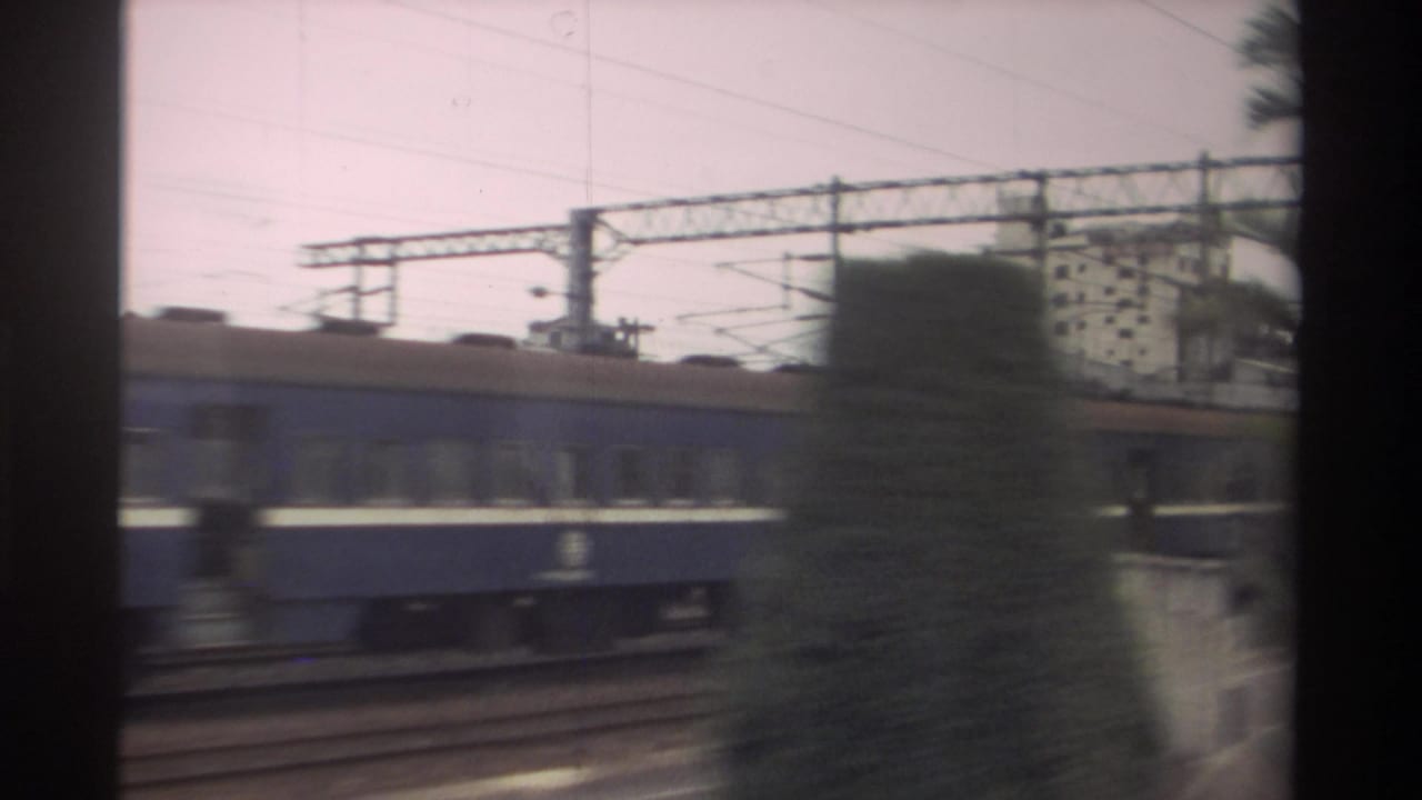 Blue passenger train passing beside tracks and overhead wires.