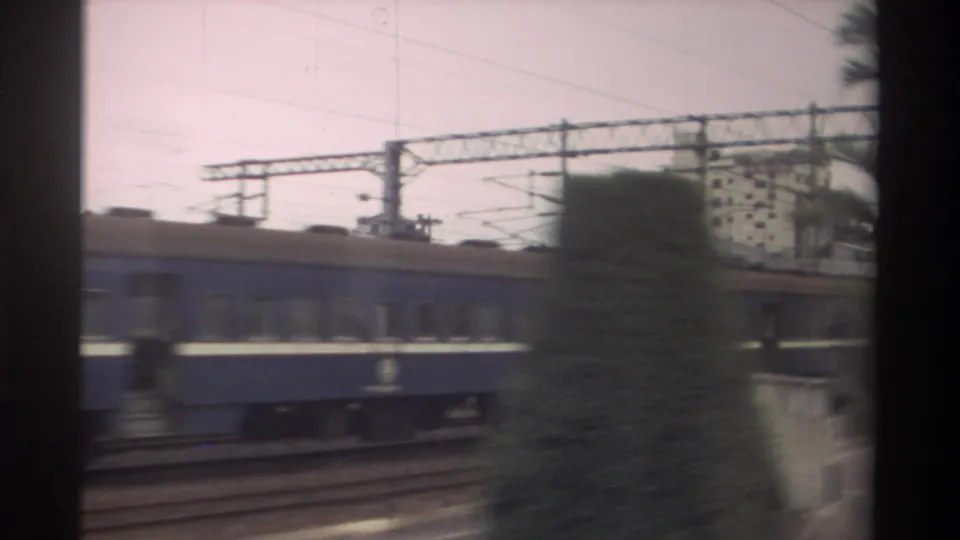 1982 Taiwan travel frame with a blue passenger train, rail tracks, overhead electrical lines, and a distant building.