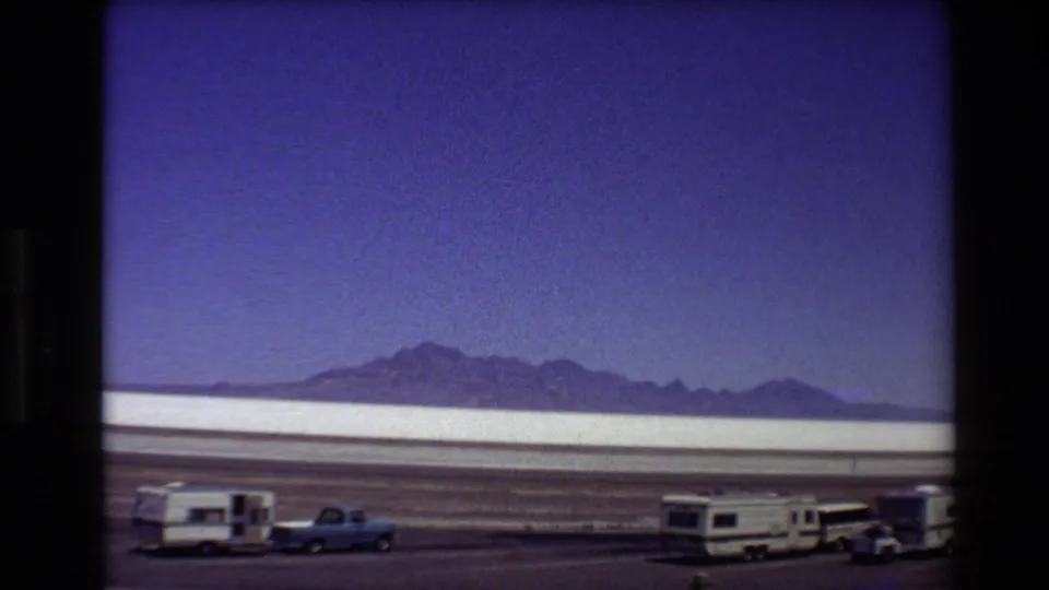 Final 8mm frame of camper trailers and pickups stopped by a Western USA salt-flat landscape in 1980.