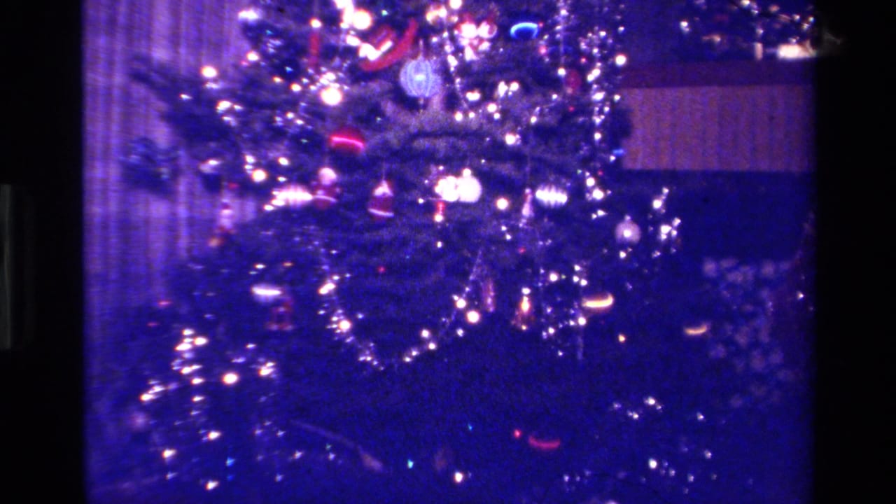 1979 California 8mm frame of a heavily decorated indoor Christmas tree with purple-blue color cast, bright bulbs, tinsel, and reflective ornaments.