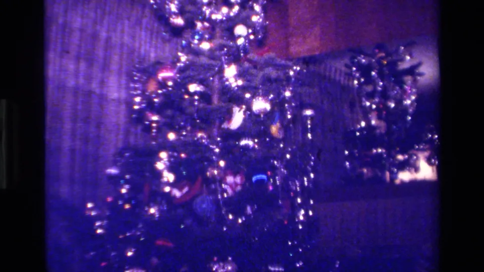 1979 California 8mm frame with a slightly tilted view of the Christmas tree, showing ornaments, tinsel, glowing bulbs, and surrounding interior surfaces.