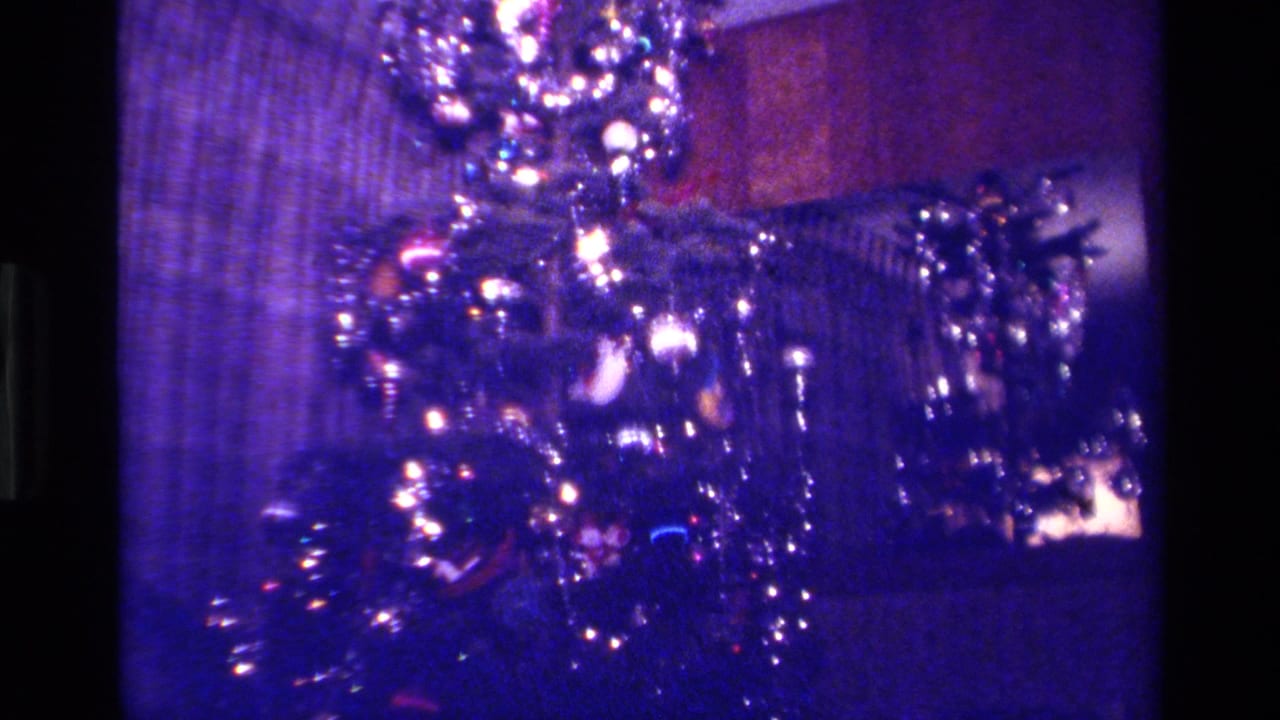 A tall decorated Christmas tree glows in a dim California home interior recorded on 8mm film in 1979.