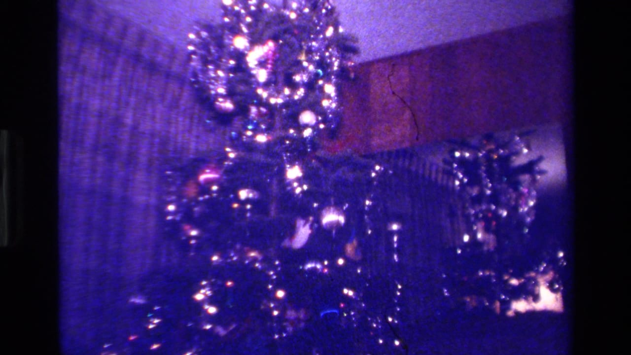 Decorated Christmas tree lights and tinsel beside a dim wall.