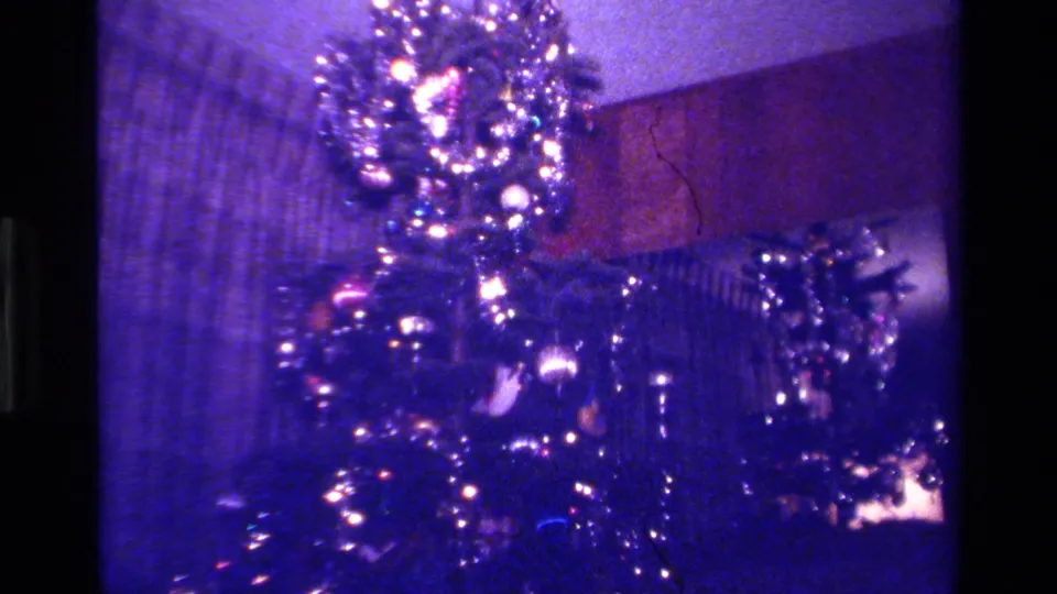 The camera holds on a lit Christmas tree with tinsel and ornaments in a 1979 California home-movie interior.