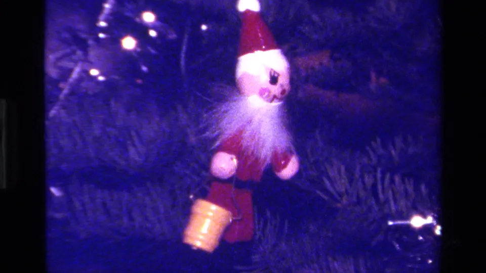 1979 California home-movie frame showing a Santa-style hanging ornament among evergreen branches, lights, and tinsel.