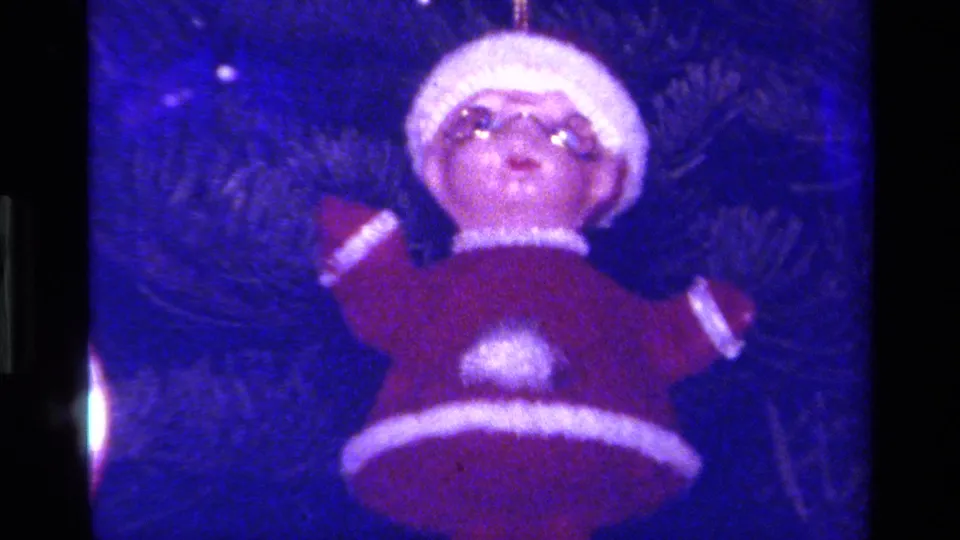 Close 8mm view of a rounded Santa ornament in red and white, suspended in front of a Christmas tree.