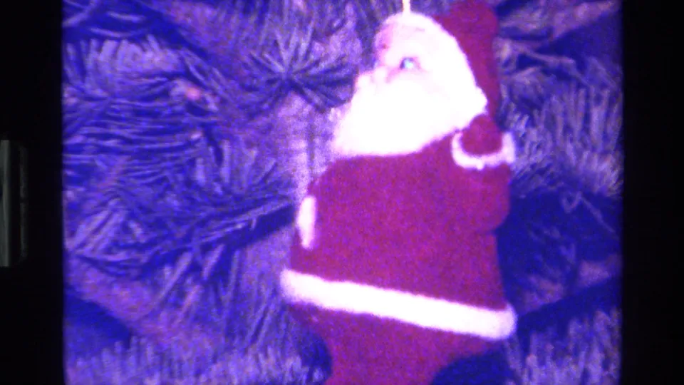 Side angle of the Santa ornament on a Christmas tree, with soft focus, pine needles, and visible 8mm color shift.