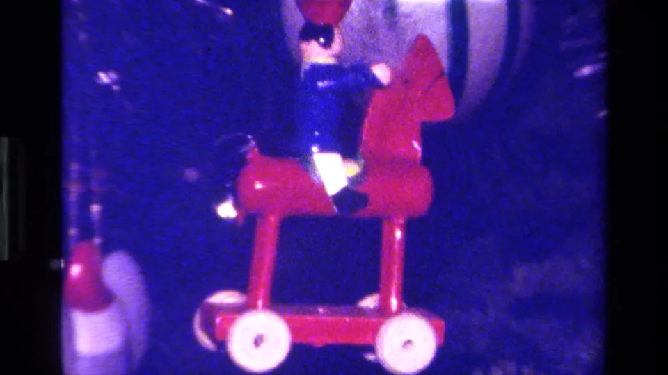 Close 8mm view of a toy soldier-like figure riding a red rocking horse ornament on a Christmas tree.