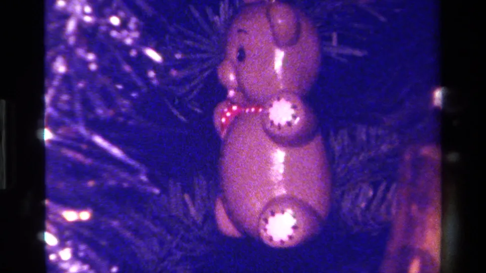 1979 home-movie close-up of a glossy bear ornament among pine needles, softened by 8mm grain and color shift.