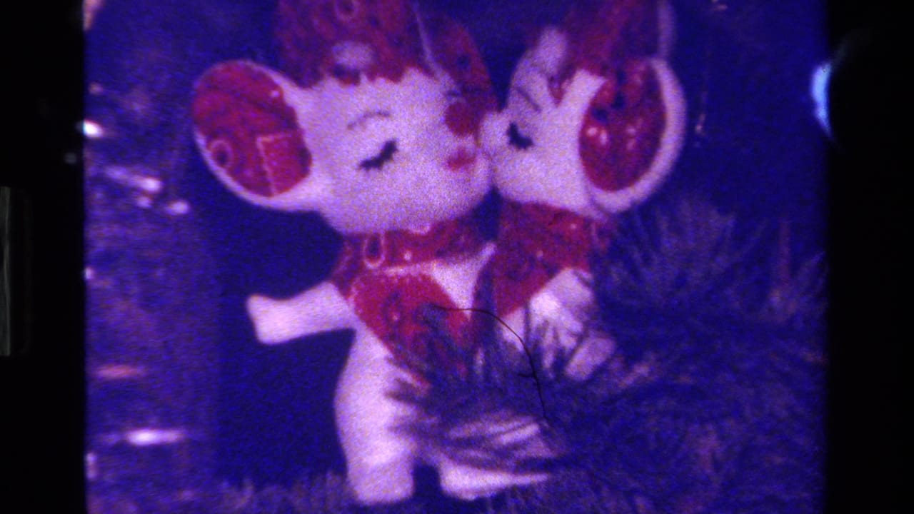 Two white mouse ornaments with red ears and scarves on a dark Christmas tree.