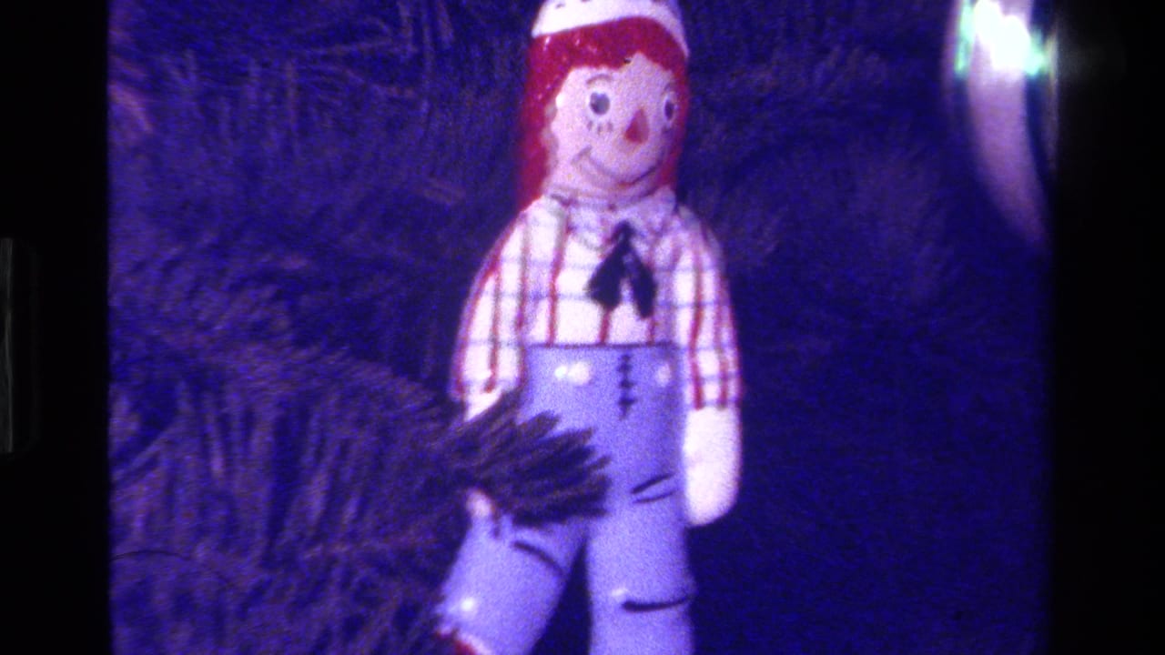 1979 California 8mm frame with a Raggedy-style cloth doll ornament in a checkered shirt and blue overalls on a dark Christmas tree.