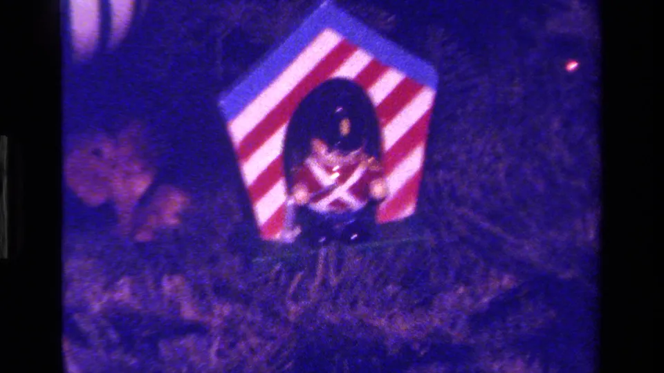 1979 California 8mm frame showing a toy soldier ornament in a red and white striped hexagonal box among evergreen branches.