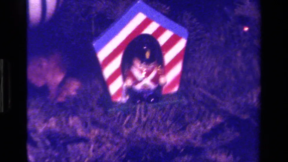 1979 California home-movie frame showing a striped red-and-white Christmas ornament nestled in pine needles.