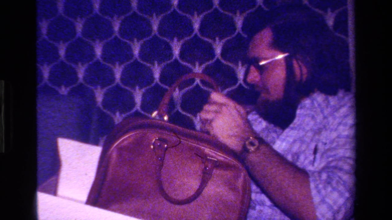 In the dim interior, the man leans forward over the brown briefcase, concentrating on the gift against blue geometric decor.