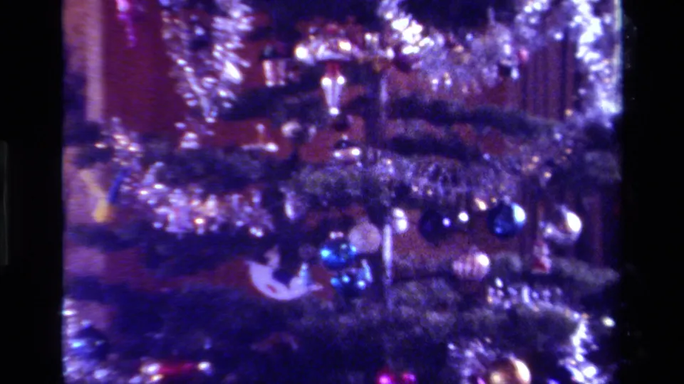 1979 California Super 8 frame of a Christmas tree detail with silver tinsel, blue baubles, and soft reflections in a dim interior.