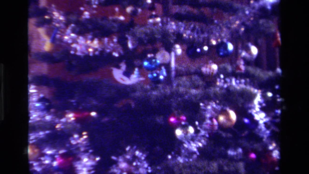1979 California home-movie still showing a tinsel-covered Christmas tree section with blue and gold ornaments under dim indoor light.